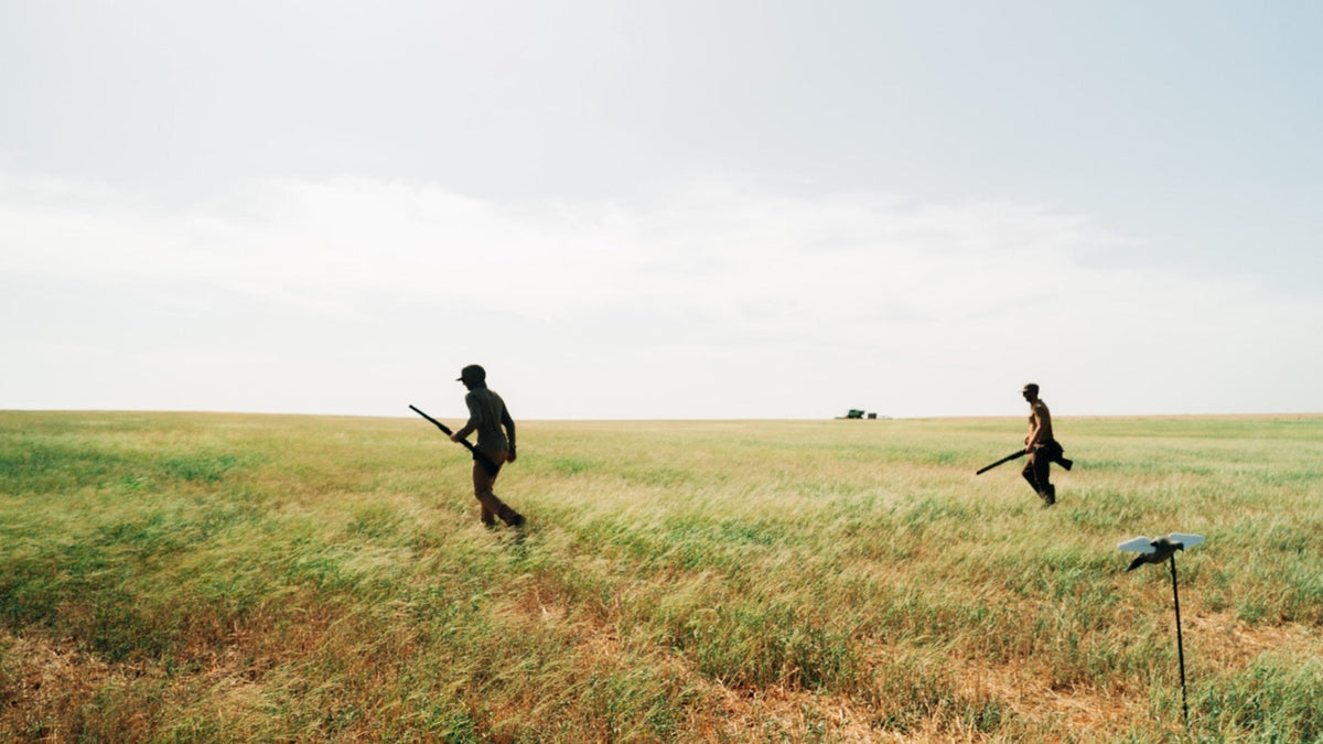 Duck Camp F26 — two hunters walking a wide field toward the decoys